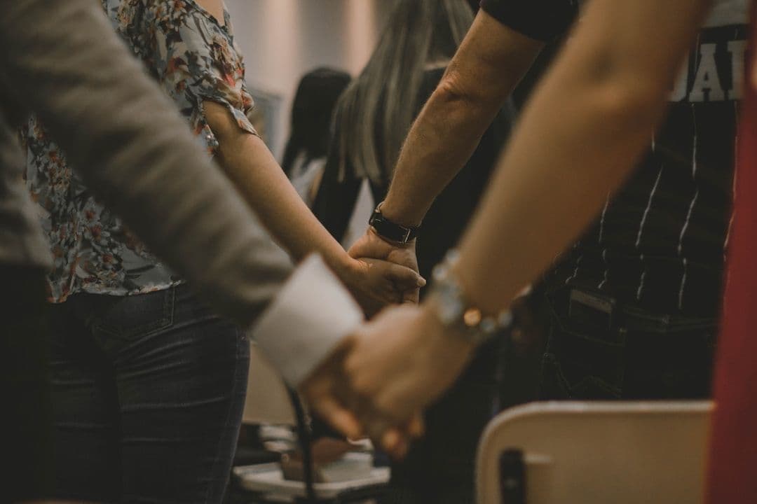 People standing in a circle, holding one another's hands in a warmly lit room.